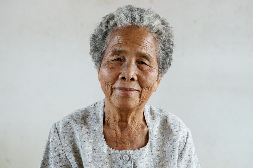 I older Asian woman with short grey hair with a soft expression and casual smile. 
