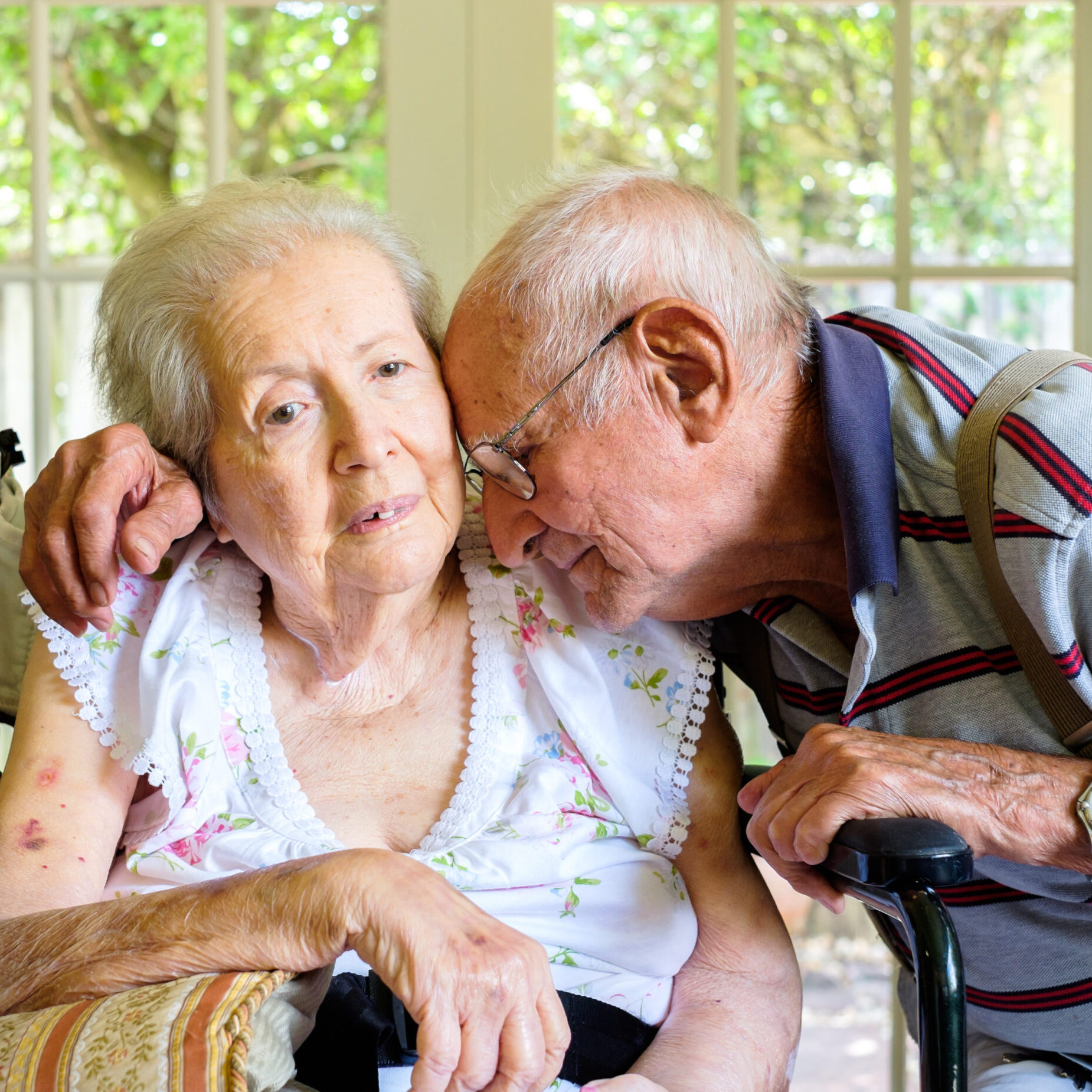 Elderly eighty plus year old woman in a wheel chair in a home setting with her husband.