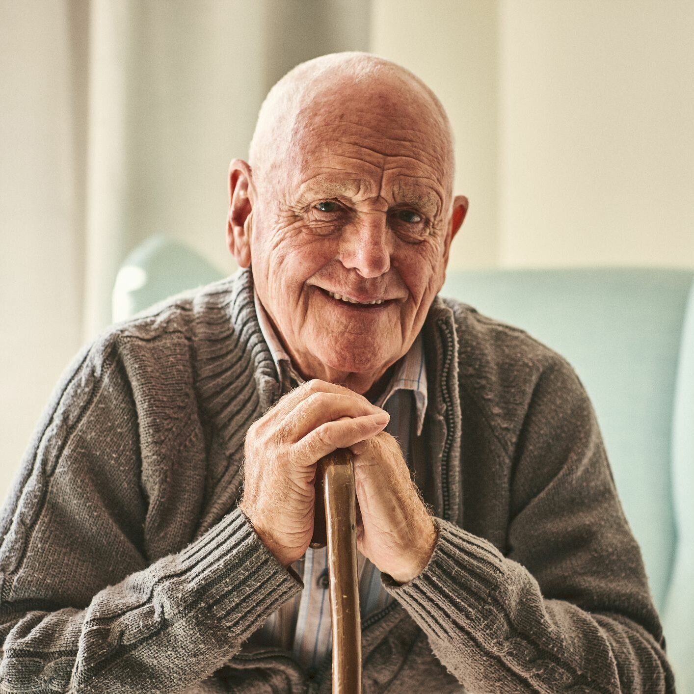 Older man smiling with his chin resting on his hands which are perched on a cane.